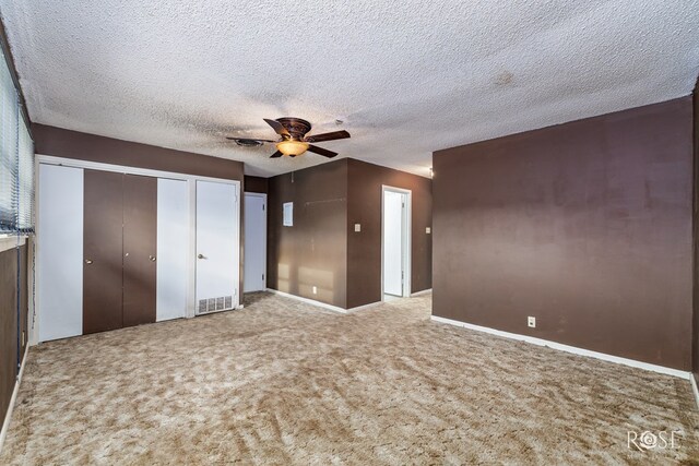 unfurnished bedroom with multiple closets, ceiling fan, carpet flooring, and a textured ceiling