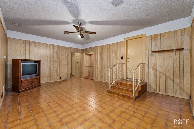 interior space with ceiling fan, light tile patterned floors, a textured ceiling, and wood walls