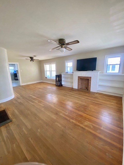 925 E 40th St, San Angelo, TX 76903 - unfurnished living room featuring wood finished floors, ceiling fan, a fireplace, and baseboards