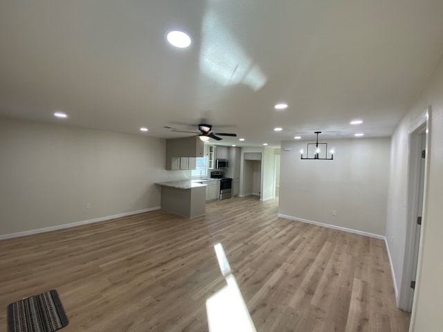 unfurnished living room with ceiling fan with notable chandelier and light hardwood / wood-style flooring