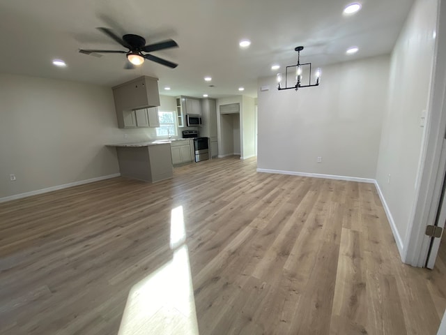 unfurnished living room featuring ceiling fan with notable chandelier and light hardwood / wood-style floors