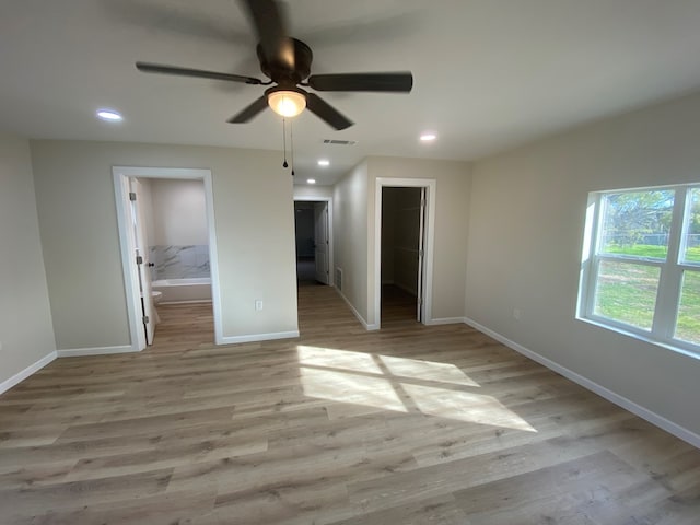 unfurnished bedroom featuring a walk in closet, ensuite bath, light wood-type flooring, a closet, and ceiling fan