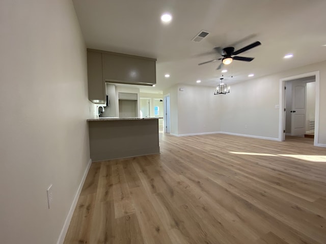 unfurnished living room with ceiling fan with notable chandelier and light hardwood / wood-style flooring