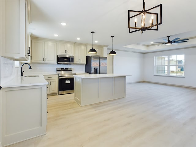 kitchen with sink, a tray ceiling, a kitchen island, pendant lighting, and stainless steel appliances