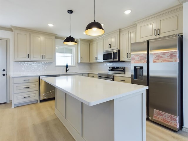 kitchen featuring sink, appliances with stainless steel finishes, hanging light fixtures, a center island, and cream cabinetry