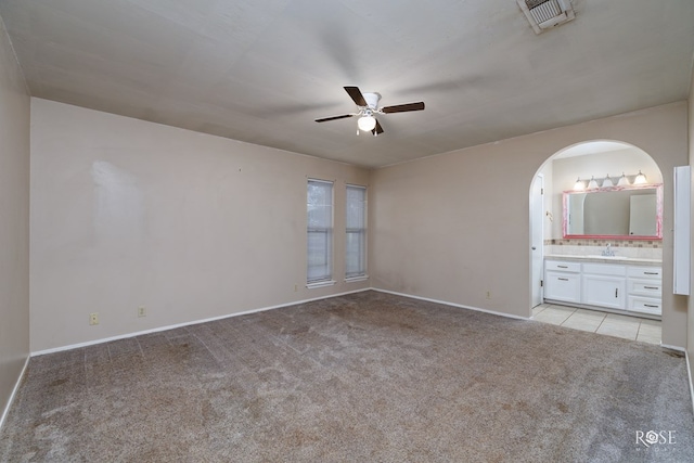 unfurnished bedroom featuring light carpet, sink, ceiling fan, and ensuite bathroom