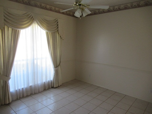 spare room with a ceiling fan, light tile patterned floors, and a healthy amount of sunlight