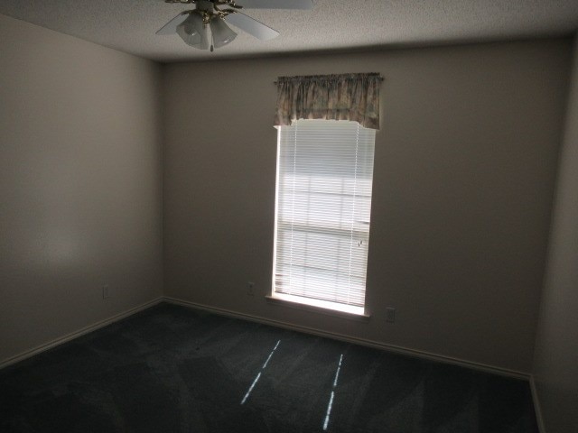unfurnished room with dark colored carpet, baseboards, a textured ceiling, and ceiling fan