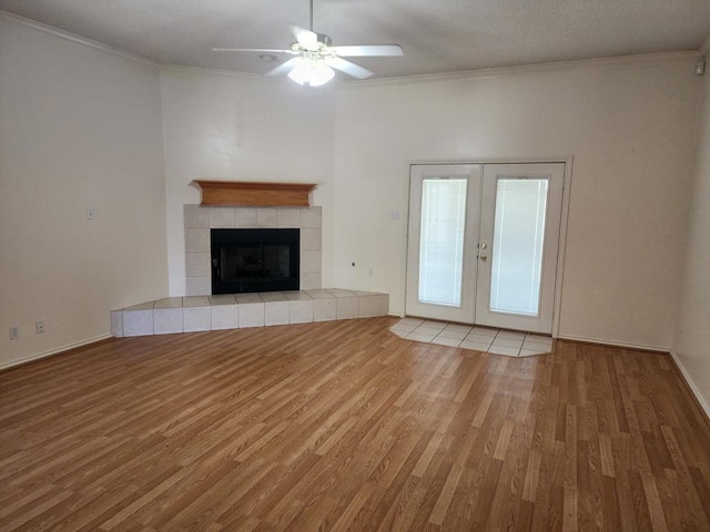 unfurnished living room featuring wood finished floors, french doors, crown molding, a fireplace, and ceiling fan