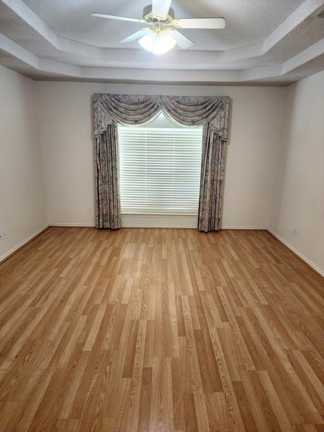 empty room featuring a ceiling fan, baseboards, light wood-style floors, and a raised ceiling