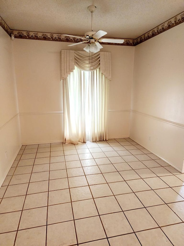empty room with a textured ceiling, baseboards, ceiling fan, and light tile patterned floors