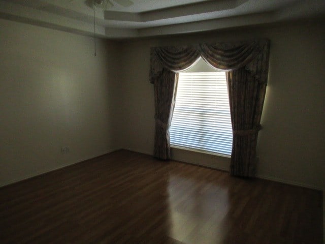 empty room featuring ceiling fan, a tray ceiling, and wood finished floors