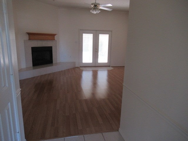 unfurnished living room with a fireplace, wood finished floors, a ceiling fan, and french doors