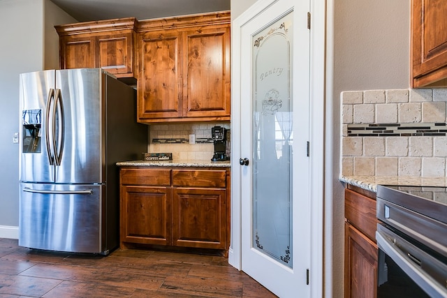 kitchen with dark hardwood / wood-style floors, tasteful backsplash, stove, light stone counters, and stainless steel refrigerator with ice dispenser