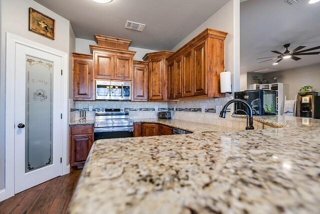 kitchen with dark wood-type flooring, ceiling fan, appliances with stainless steel finishes, backsplash, and light stone counters