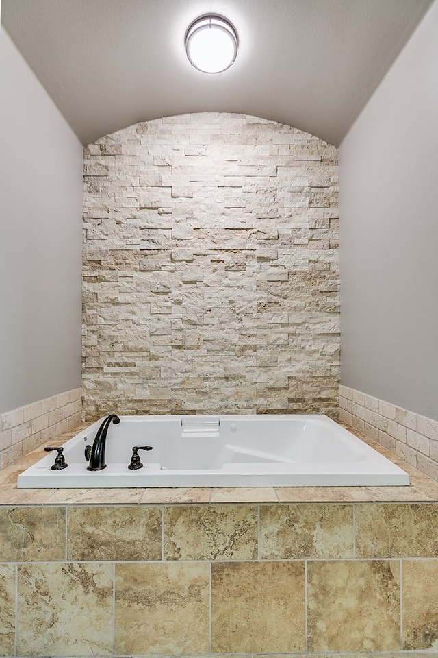 bathroom featuring lofted ceiling and tiled bath