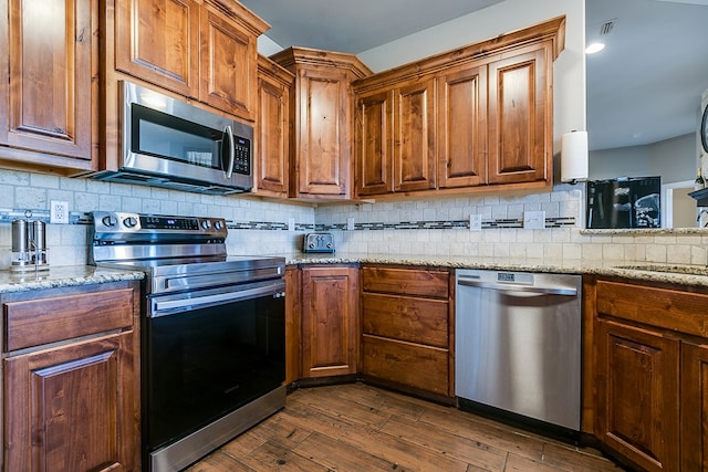 kitchen with sink, light stone counters, appliances with stainless steel finishes, dark hardwood / wood-style floors, and decorative backsplash