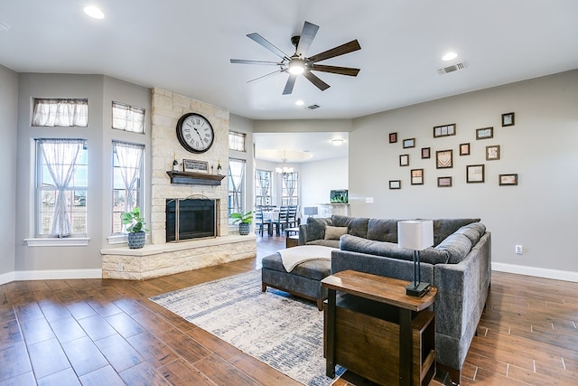 living room with a fireplace, ceiling fan with notable chandelier, and dark wood-type flooring