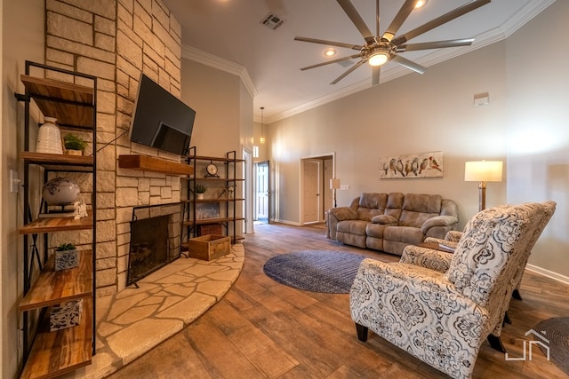 living room with crown molding, wood-type flooring, a stone fireplace, and ceiling fan