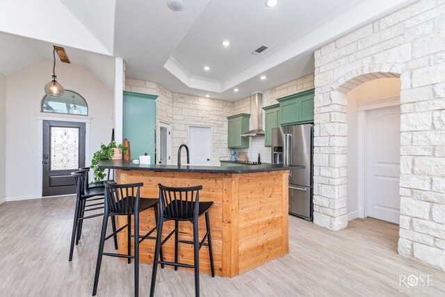 kitchen featuring high end fridge, a breakfast bar, wall chimney exhaust hood, and green cabinets