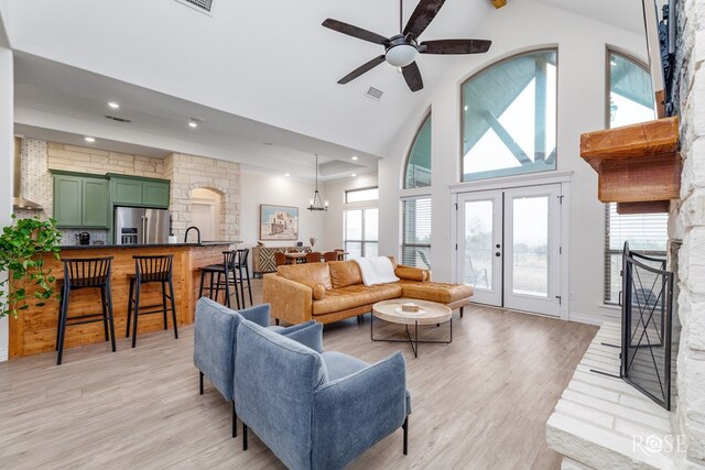 living room with a fireplace, high vaulted ceiling, ceiling fan, and light wood-type flooring