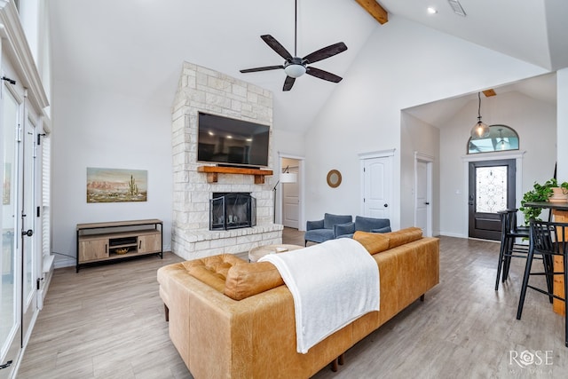 living room featuring a stone fireplace, high vaulted ceiling, light hardwood / wood-style floors, and beamed ceiling