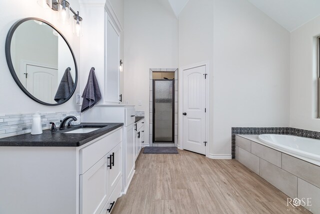 bathroom featuring high vaulted ceiling, vanity, a relaxing tiled tub, hardwood / wood-style floors, and backsplash