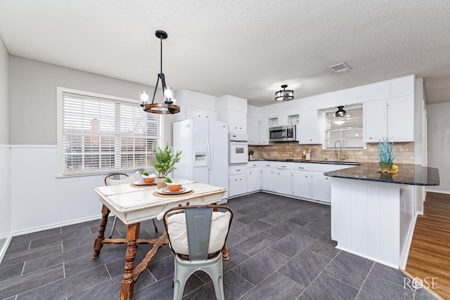 kitchen featuring white appliances, hanging light fixtures, white cabinetry, and sink