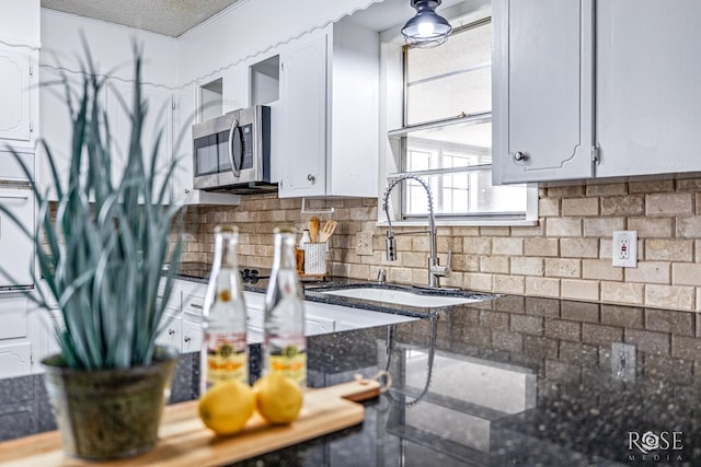 kitchen with a textured ceiling, backsplash, sink, white cabinetry, and dark stone countertops