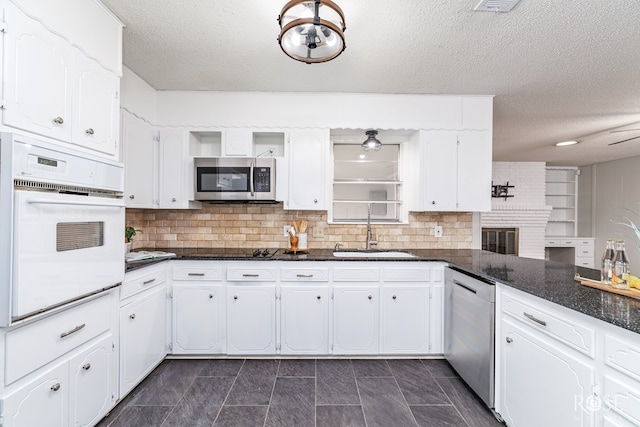 kitchen with appliances with stainless steel finishes, sink, backsplash, white cabinetry, and dark stone counters