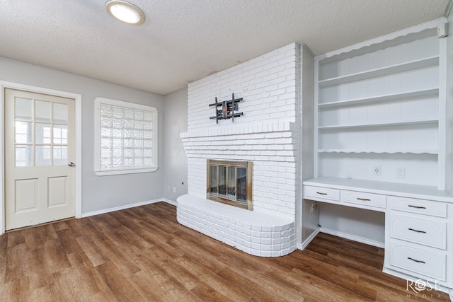 unfurnished living room with a brick fireplace, a textured ceiling, dark hardwood / wood-style flooring, and built in desk