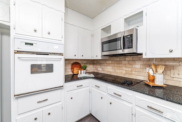 kitchen featuring black electric cooktop, oven, white cabinetry, and dark stone counters