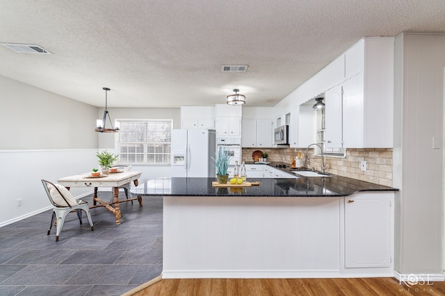 kitchen with decorative light fixtures, sink, white refrigerator with ice dispenser, and kitchen peninsula