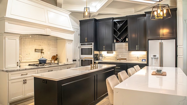 kitchen with pendant lighting, sink, appliances with stainless steel finishes, a kitchen island with sink, and light stone countertops