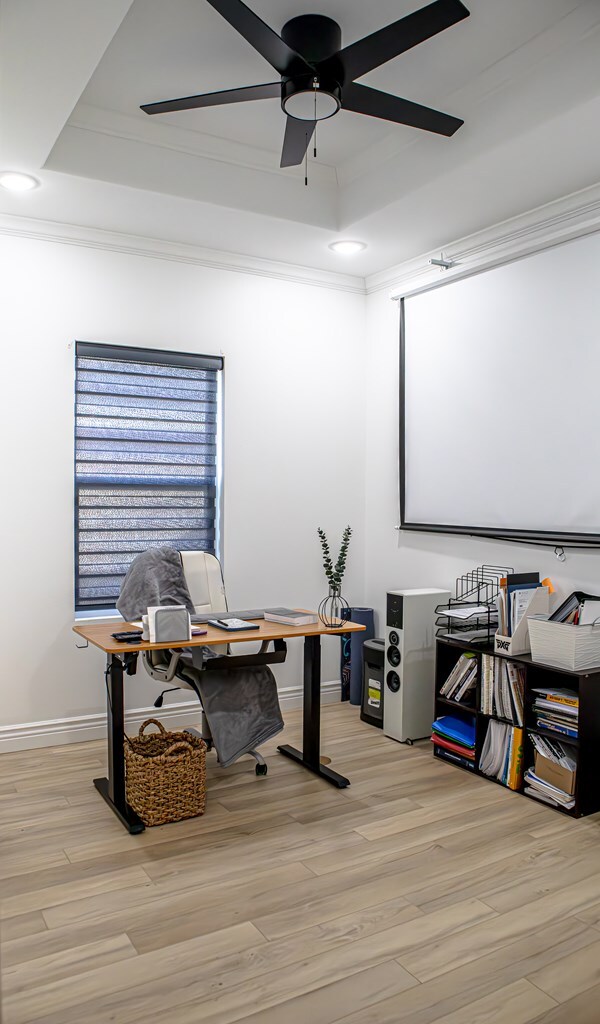 office area featuring crown molding, a tray ceiling, light hardwood / wood-style floors, and ceiling fan