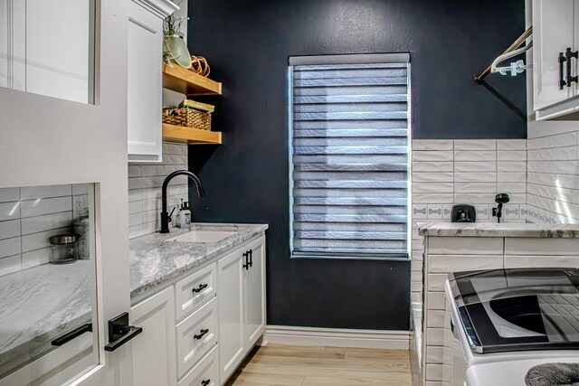 kitchen featuring sink, white cabinetry, light hardwood / wood-style flooring, washer and dryer, and light stone countertops