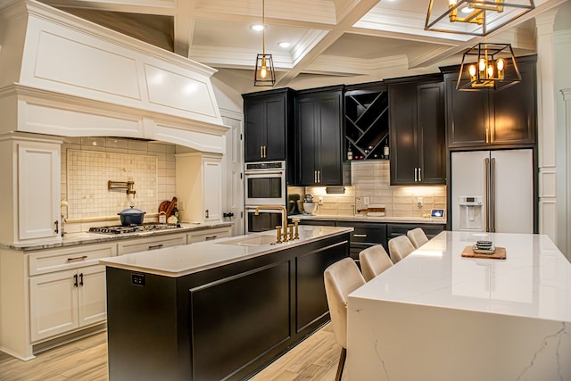 kitchen featuring appliances with stainless steel finishes, pendant lighting, an island with sink, sink, and light hardwood / wood-style flooring