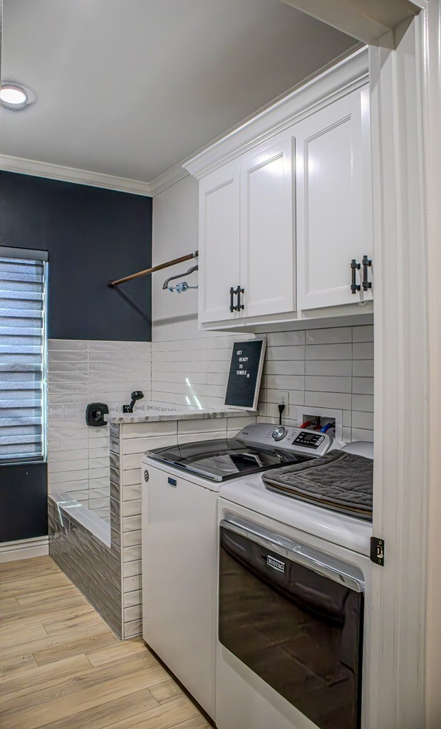 laundry area featuring washer and dryer, light hardwood / wood-style floors, ornamental molding, and cabinets