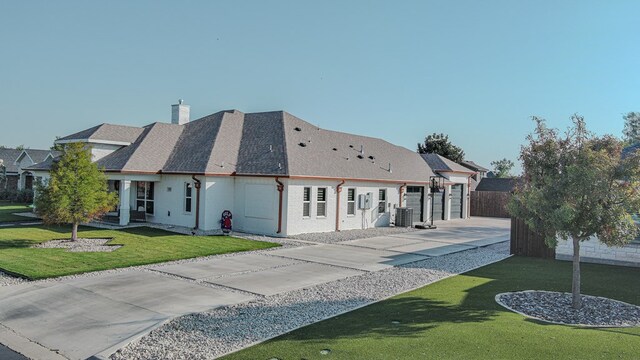 rear view of property with a garage, cooling unit, and a lawn