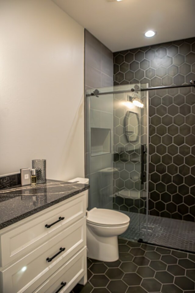 bathroom with tile patterned flooring, vanity, toilet, and a tile shower