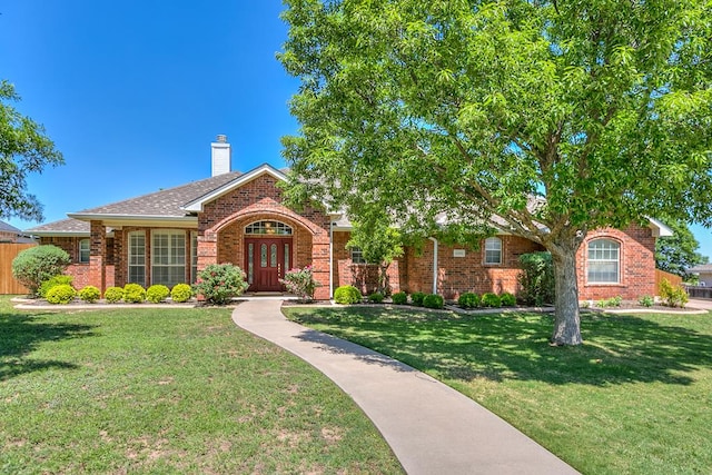 view of front facade with a front lawn, a chimney, brick siding, french doors, and fence