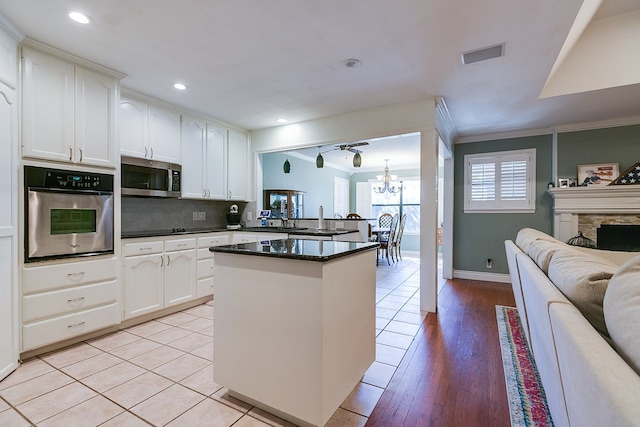 kitchen with appliances with stainless steel finishes, white cabinets, ornamental molding, a notable chandelier, and light wood-type flooring