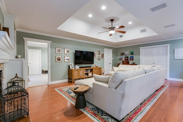 living room featuring ceiling fan, a tray ceiling, a fireplace, ornamental molding, and wood-type flooring