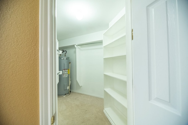 walk in closet featuring water heater and light colored carpet