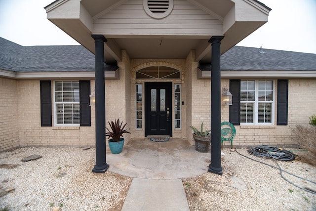 view of exterior entry with a shingled roof and brick siding