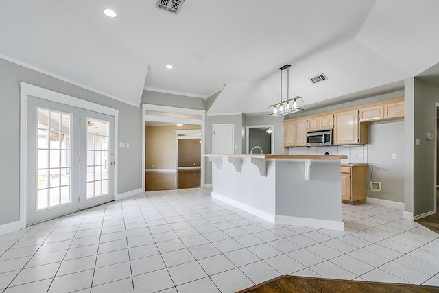 kitchen with light countertops, stainless steel microwave, visible vents, light brown cabinets, and a kitchen bar