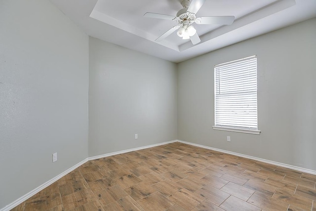 unfurnished room with light wood finished floors, ceiling fan, baseboards, and a raised ceiling