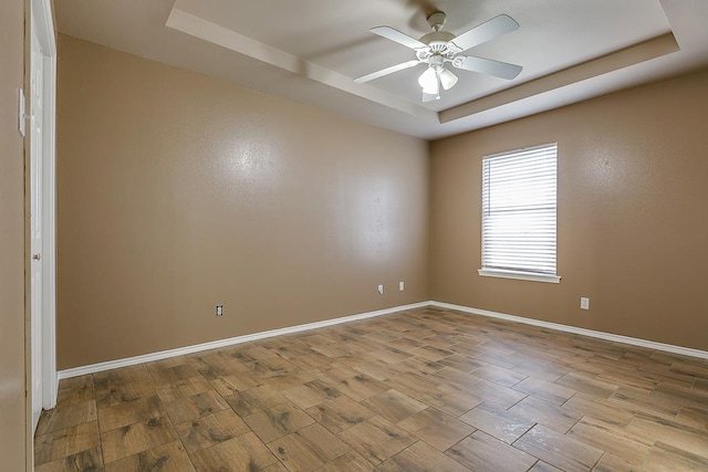 empty room featuring light wood-style floors, a raised ceiling, ceiling fan, and baseboards