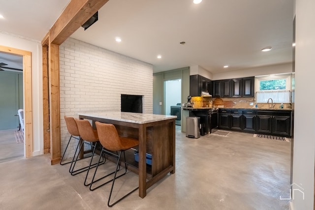 kitchen with a breakfast bar, sink, light stone counters, kitchen peninsula, and brick wall