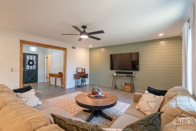 living room featuring ceiling fan, ornamental molding, and wooden walls